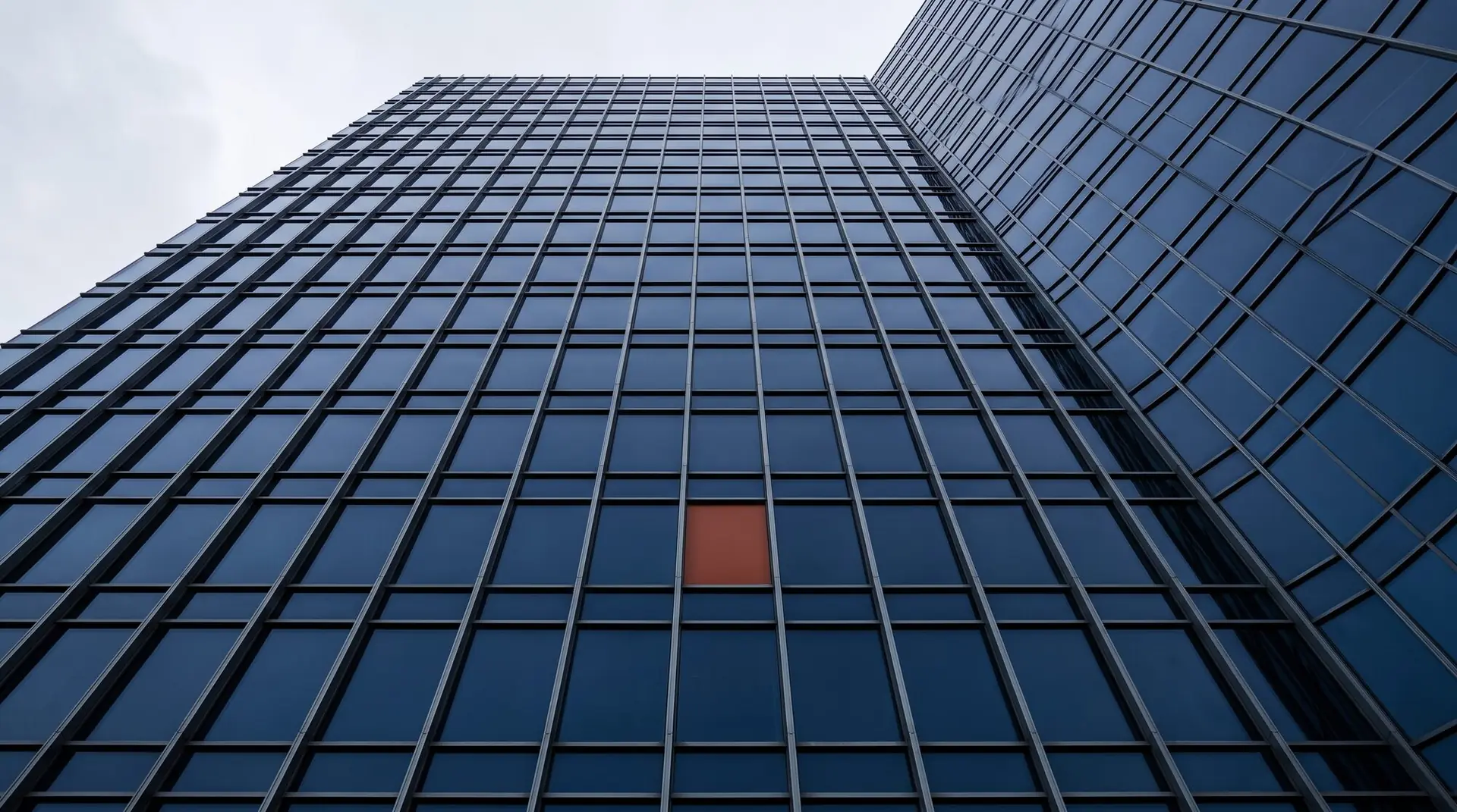 Glass office facade with rows of perfectly aligned panels and a single red panel